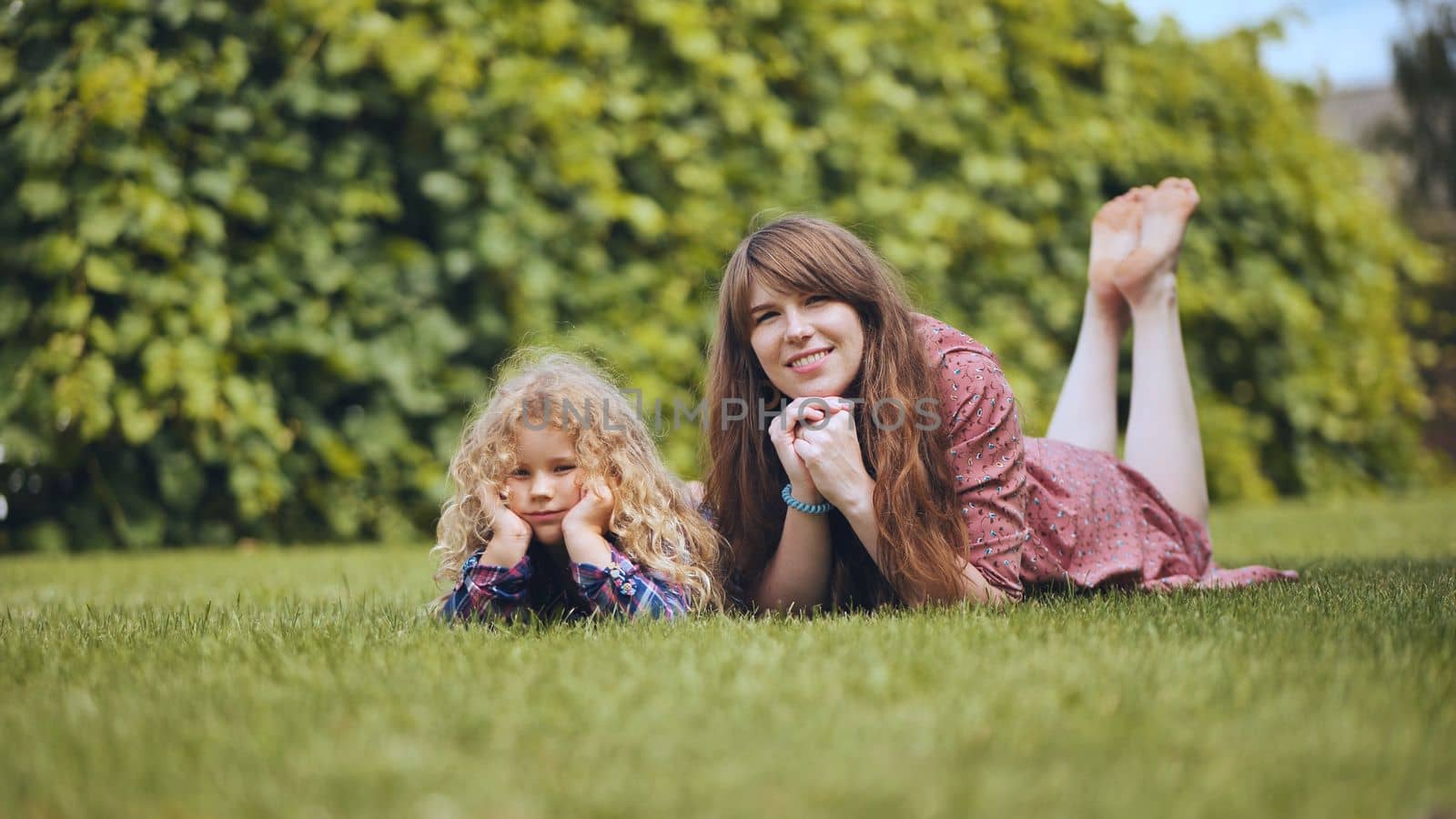 A mother and her daughter lie on the grass in the garden. by DovidPro