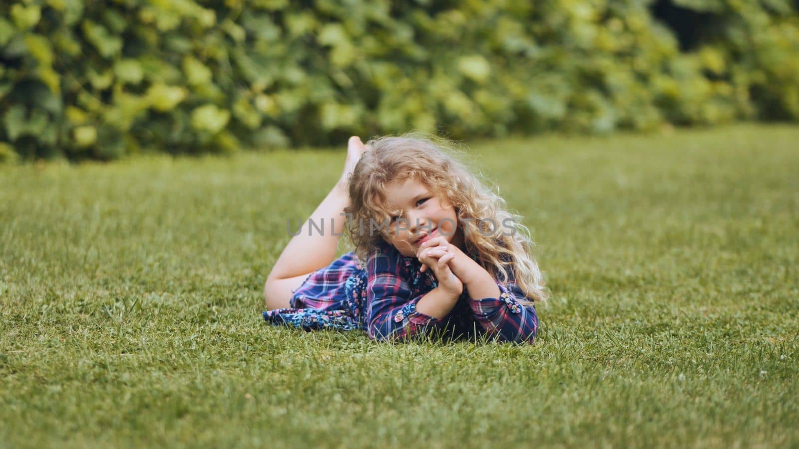 A little curly-haired girl lies on the grass in the garden