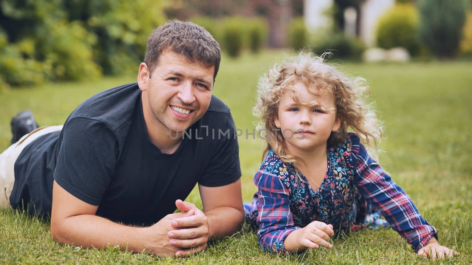 A father kisses his young daughter in the garden while lying on the grass