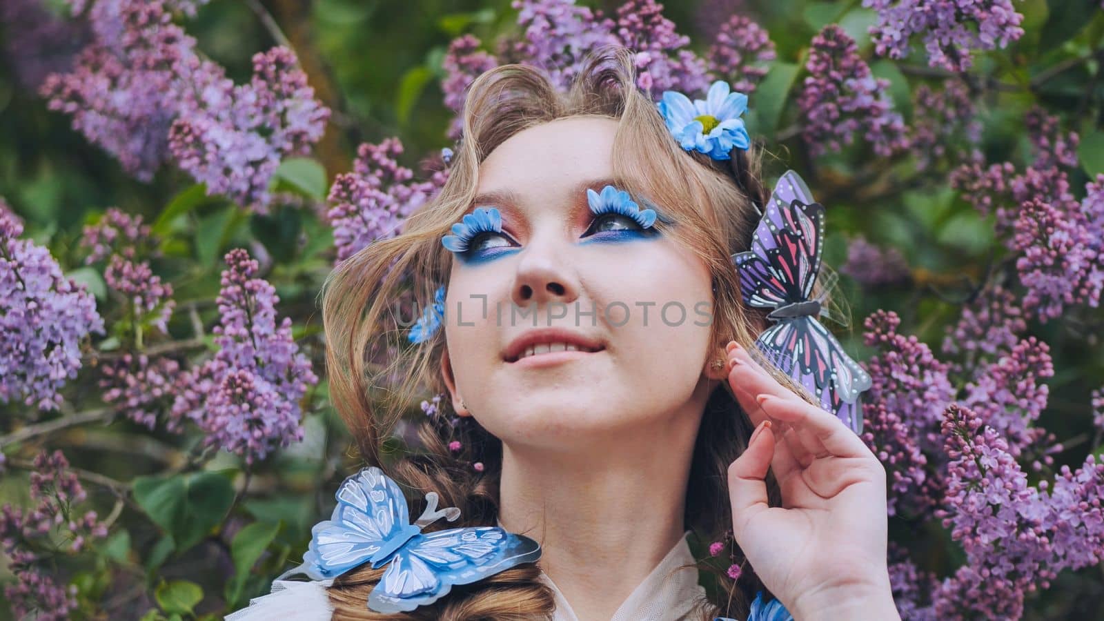 A young girl poses in lilac with a beautiful hairstyle of flowers and butterflies