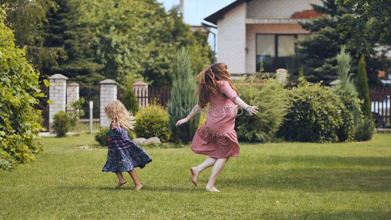 A mother and her daughter twirl in the garden outside the house