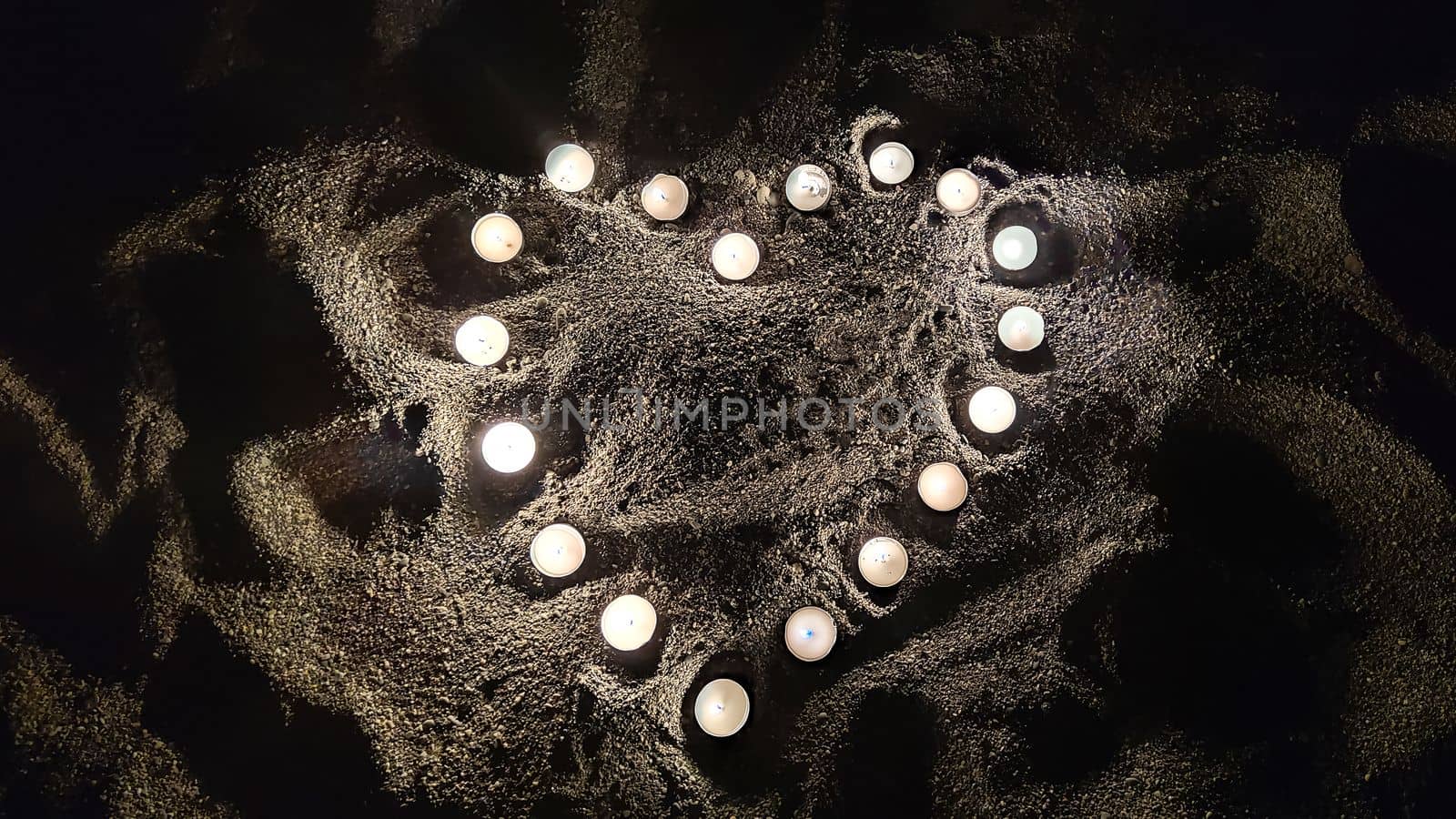 Heart made of small burning candles on sand in dark, concept of love and Valentine's Day