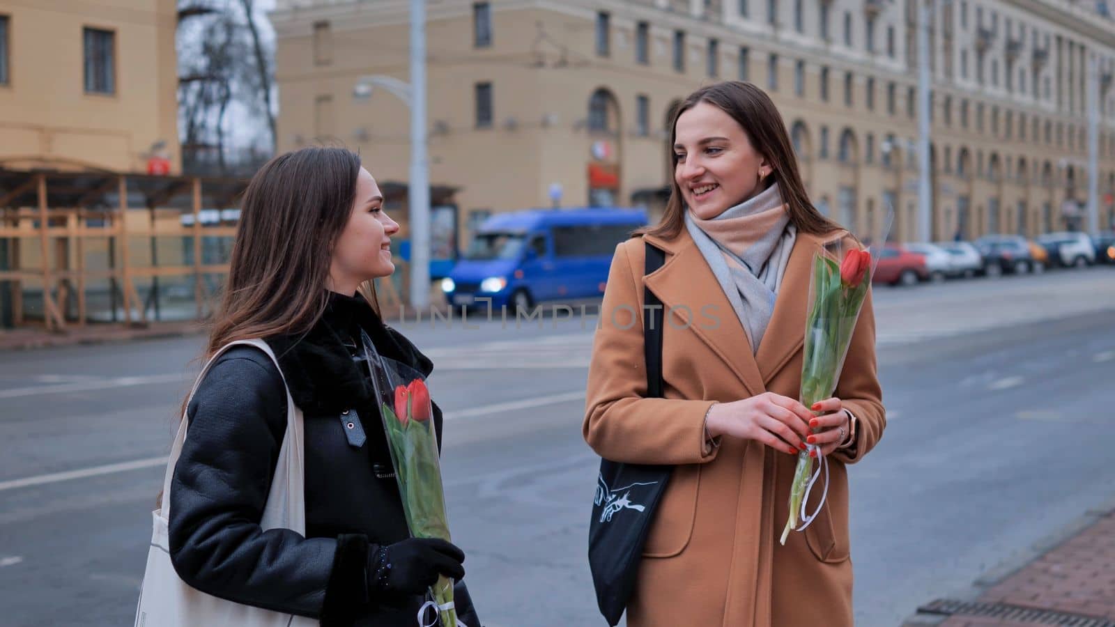 Two cheerful girlfriends say goodbye to each other on a city street. by DovidPro