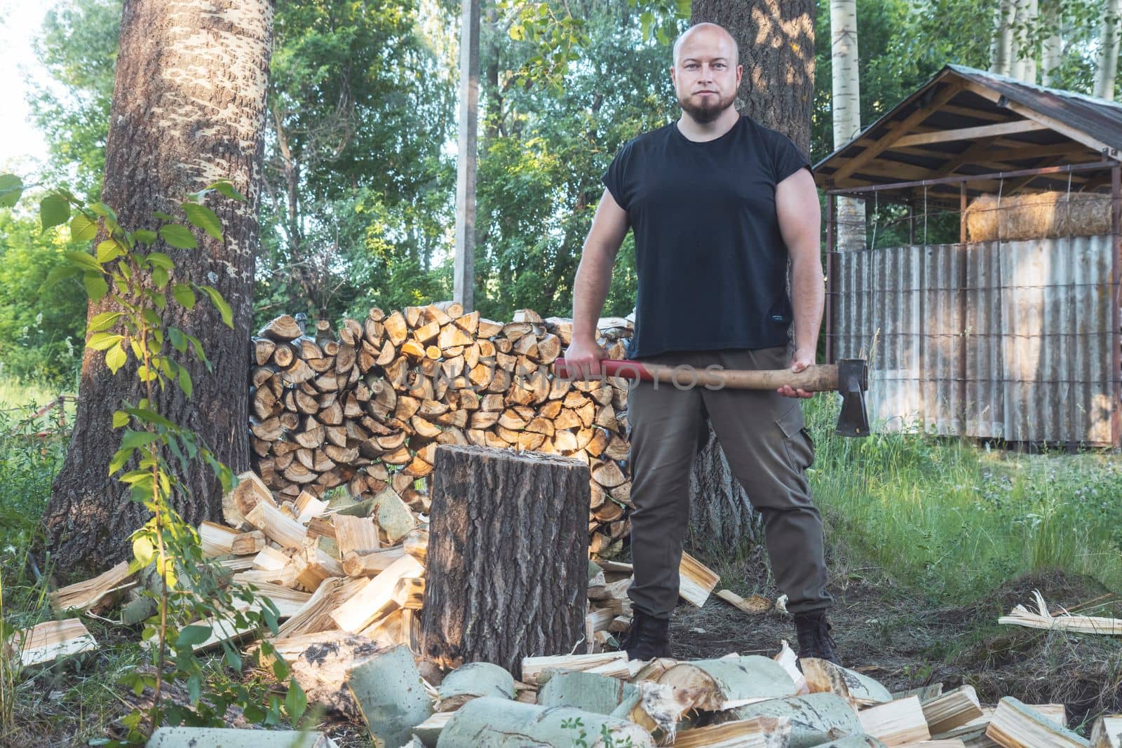 lumberjack stands with an ax near the chopped firewood , timber harvesting