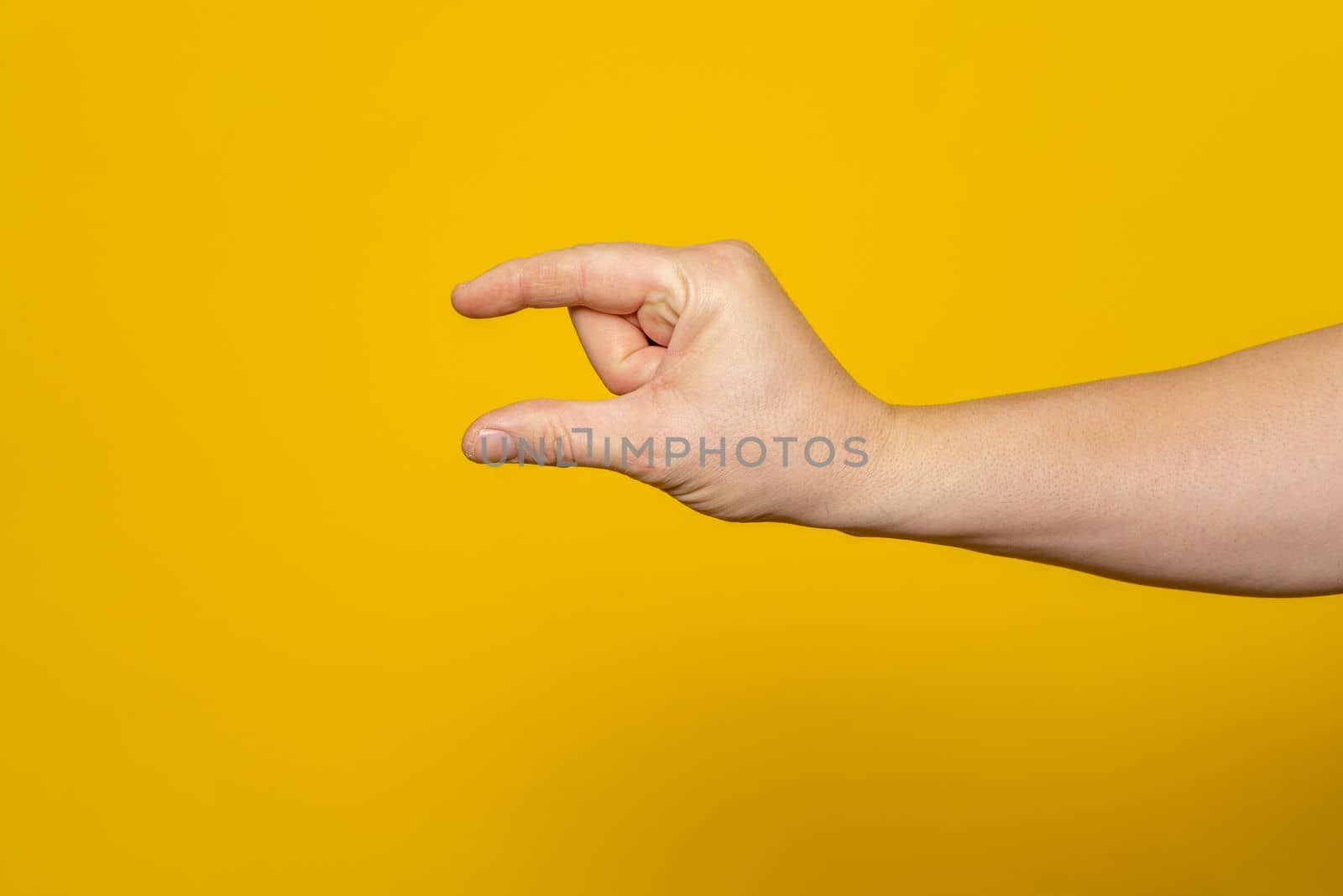 Sturdy man's hand making the small amount gesture isolated on yellow background