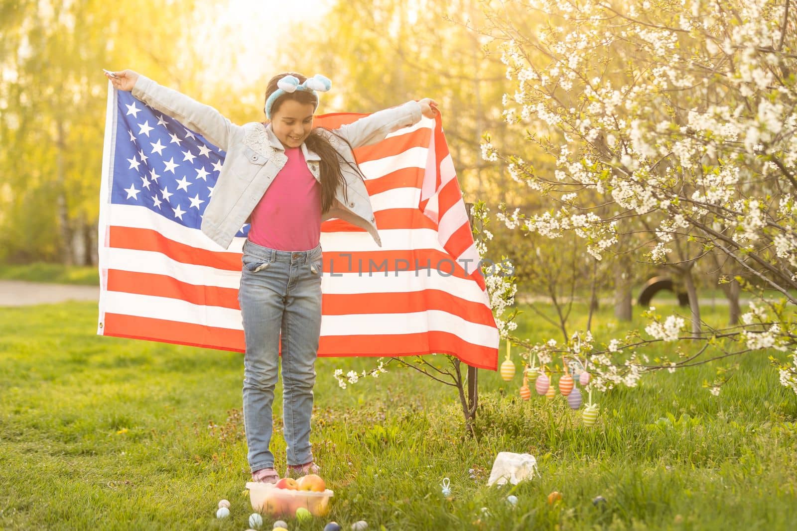 Girl kid in rabbit bunny ears on head with colored eggs and american flag. easter by Andelov13