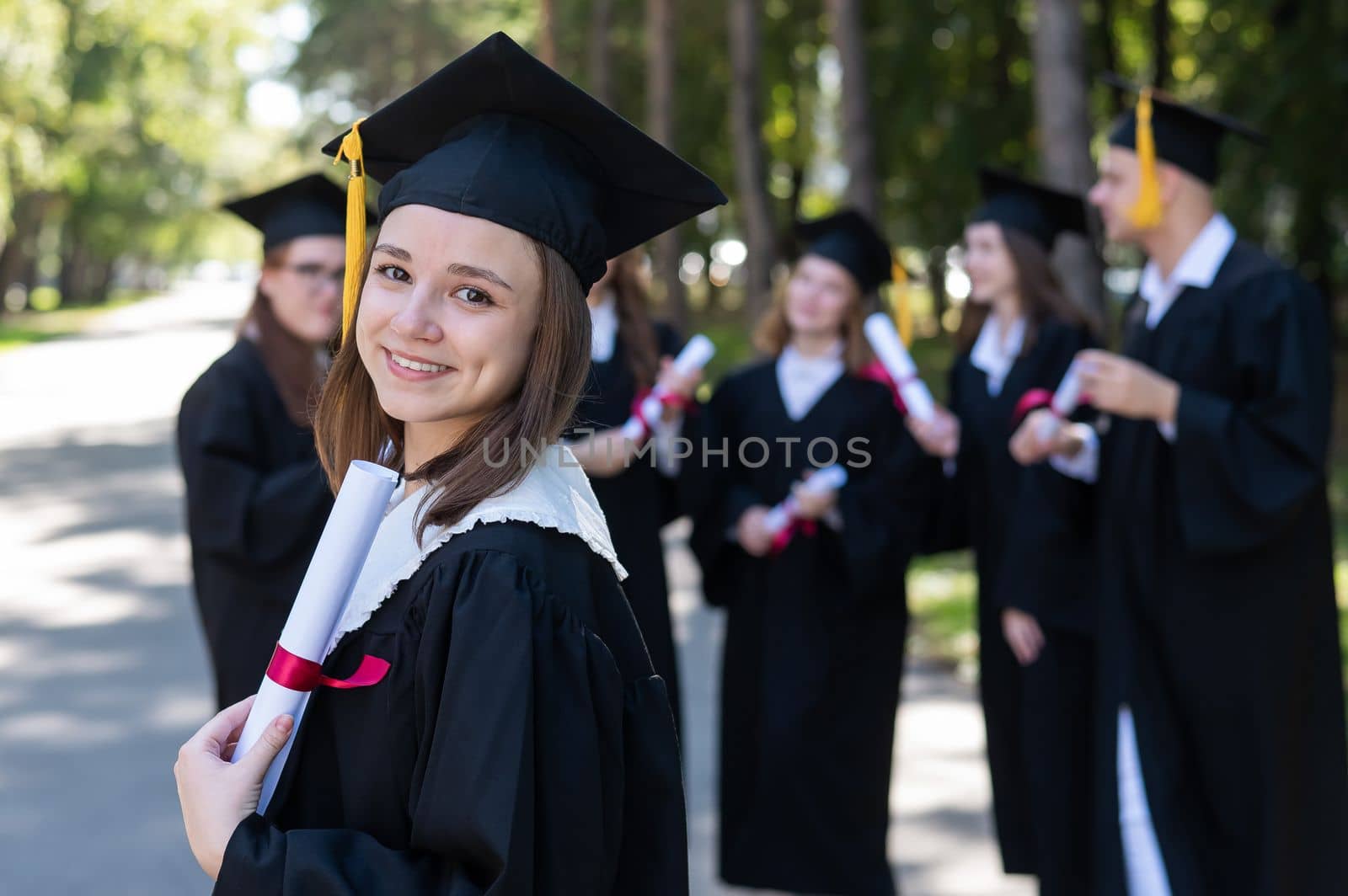Group of happy students in graduation gowns outdoors. A young girl is happy to receive her diploma. by mrwed54