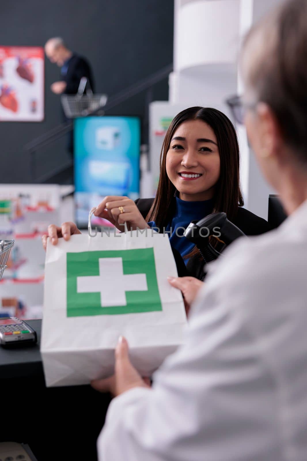 Staisfied asian customer taking drugstore order package at counter by DCStudio