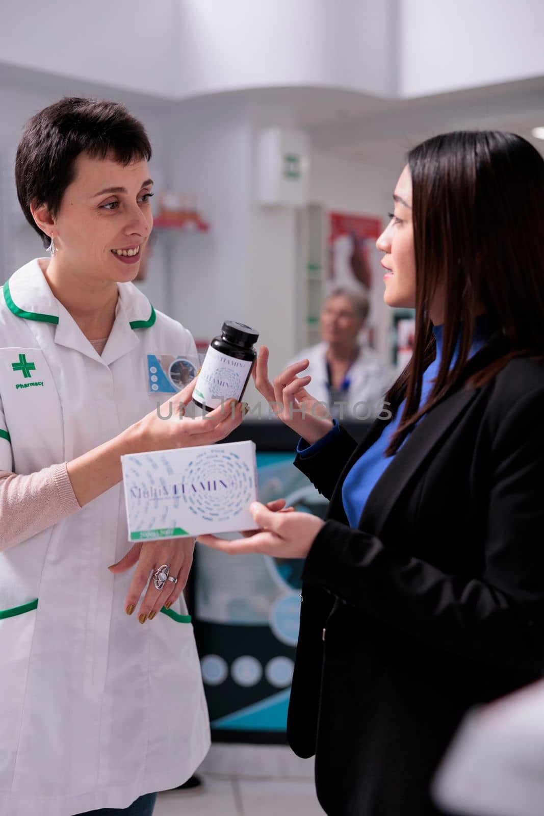 Pharmaceutical specialist discussing multivitamin healthcare benefit with customer in drugstore. Young asian woman choosing between two vitamin packages in pharmacy store