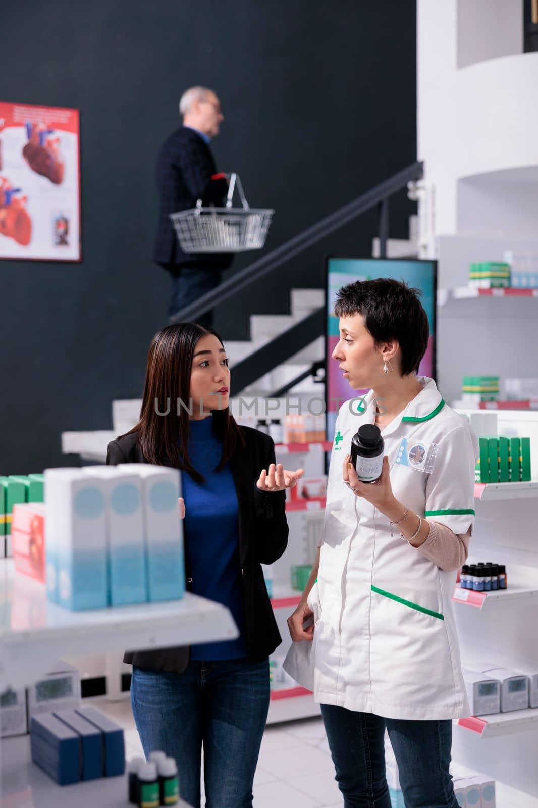 Asian woman buying vitamin and consulting with pharmacy worker by DCStudio