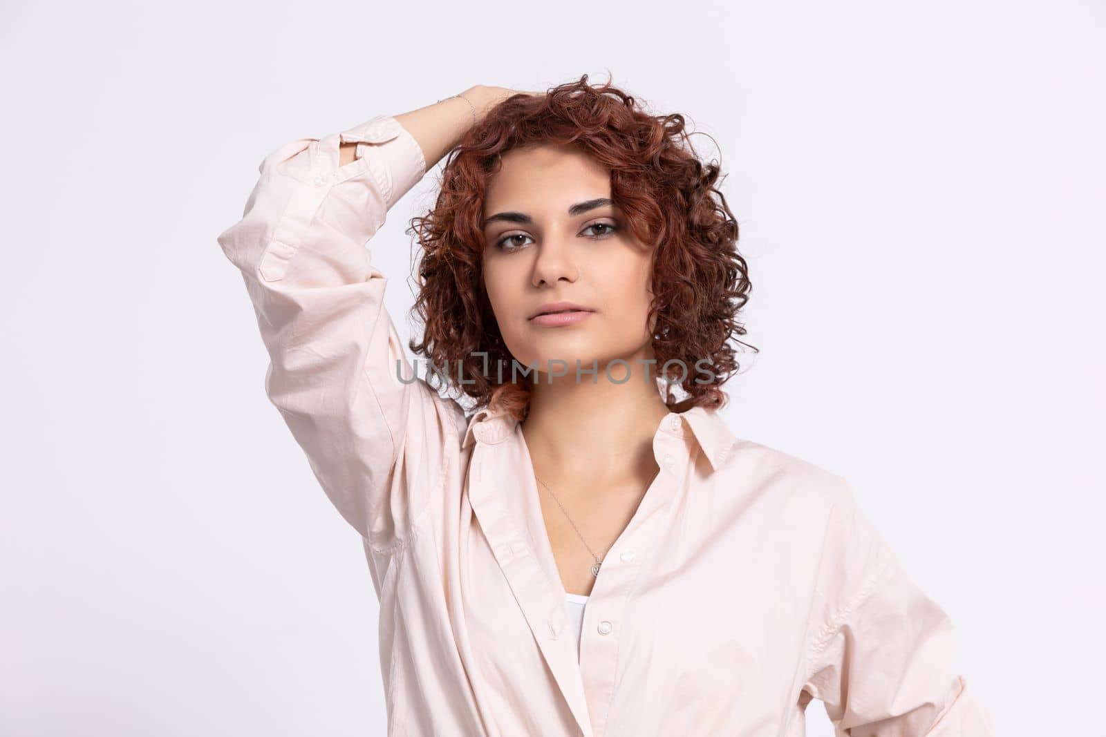 A young girl with short curly chestnut-colored hair. Hand carried up to head height. Light-colored long-sleeved blouse.