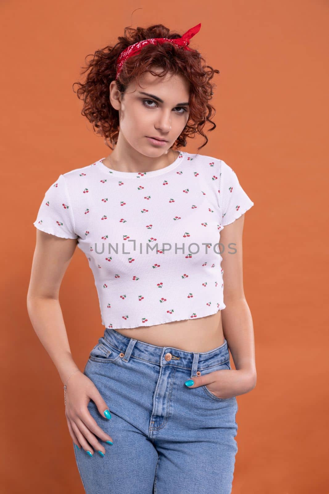 The menacing look of a young girl. Curly chestnut-colored hair. European woman with light Caucasian skin complexion. Isolated from the uniform background.