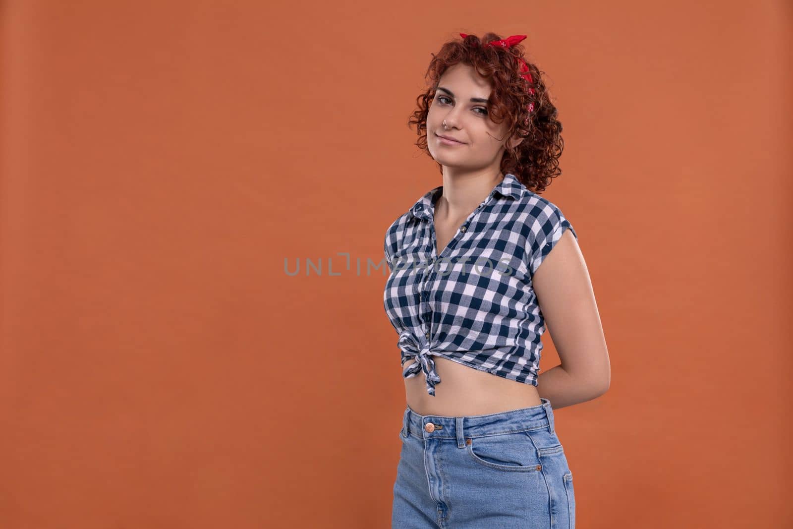 Young girl dressed in pin up style. Checkered shirt. Isolated from a solid background of brick color. Short curly hair in chestnut color.