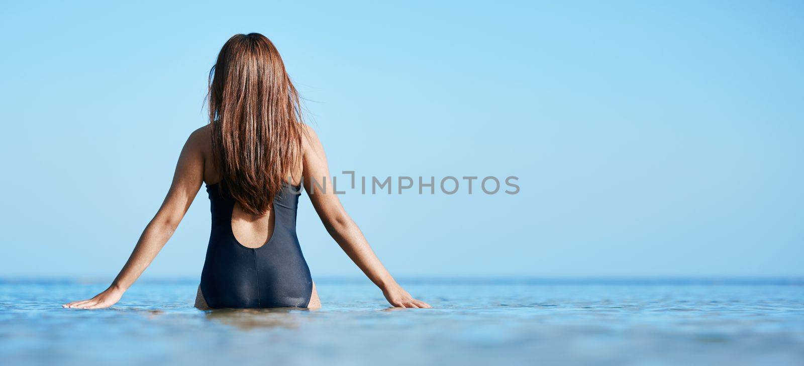 Back, young woman swimming at the beach on vacation in Mauritius and horizon of blue ocean water in summer. Calm female tourist in sea, freedom of travel lifestyle or relaxing on coastal destination by YuriArcurs