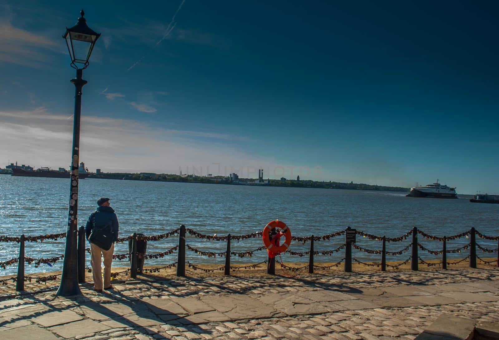 LIVERPOOL UK - May 13, 2019 - The young man stood alone under the Street lamp on the river walk in Royal Albert Dock, Liverpool