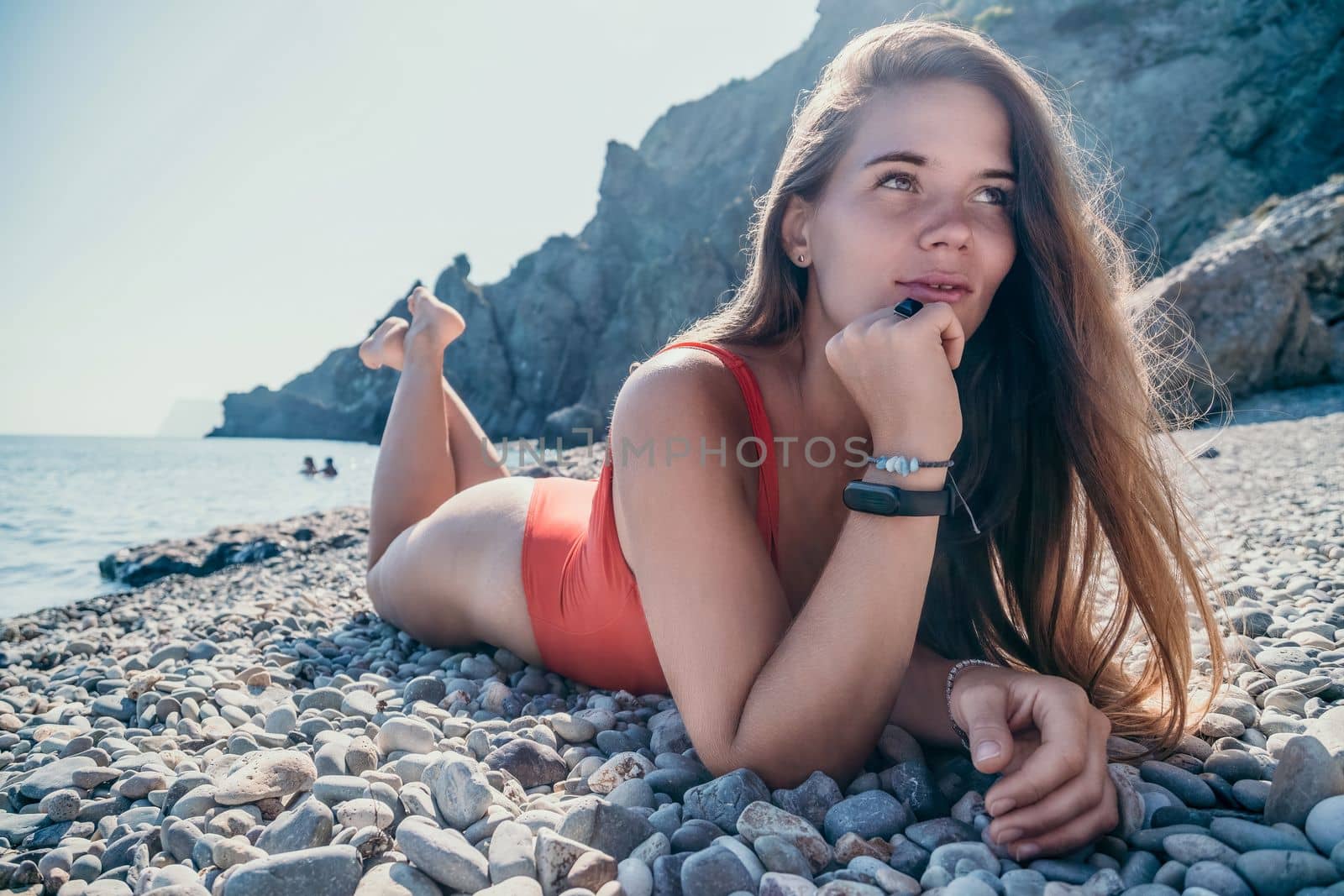 Young woman in red bikini on Beach. Girl lying on pebble beach and enjoying sun. Happy lady with long hair in bathing suit chilling and sunbathing by turquoise sea ocean on hot summer day. Close up by panophotograph