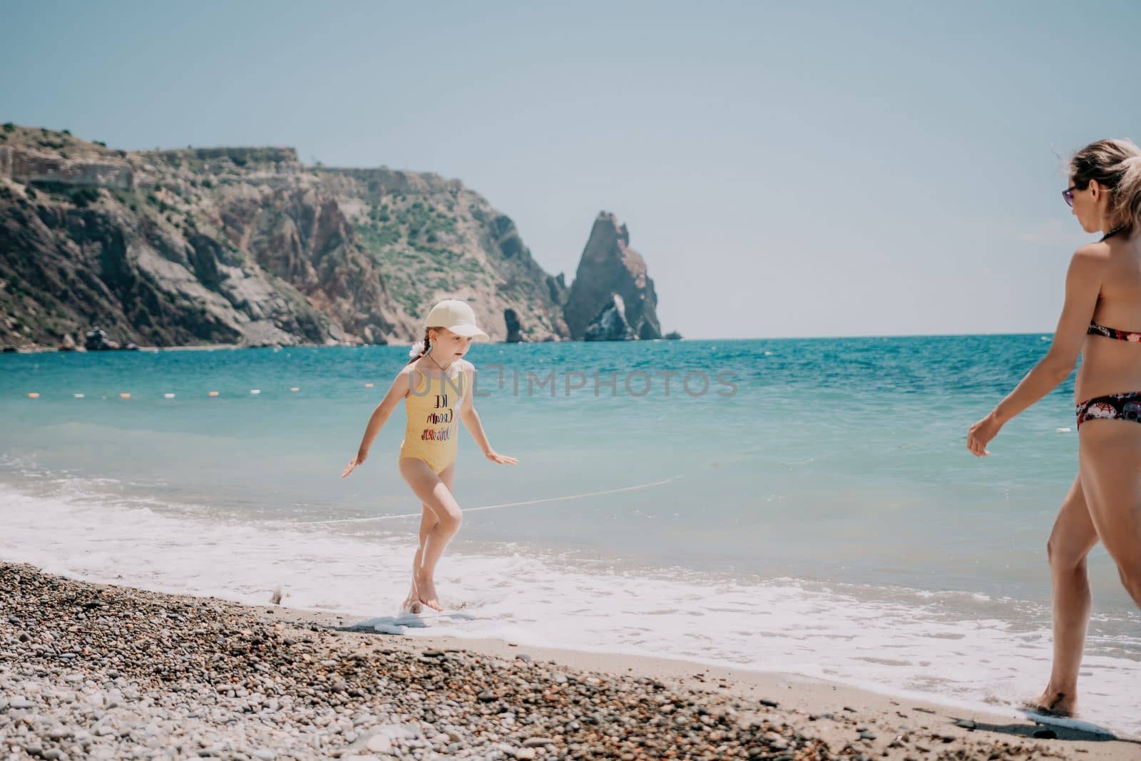 Cute little girl running along the seashore against a clear blue sea and rejoices in the rays of the summer sun. Beautiful girl in yellow swimsuit running and having fun on tropical beach