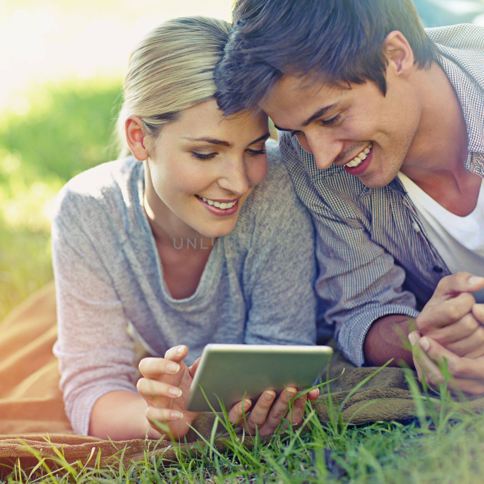 Love on the lawn. a happy young couple lying on the grass and using a digital tablet together. by YuriArcurs
