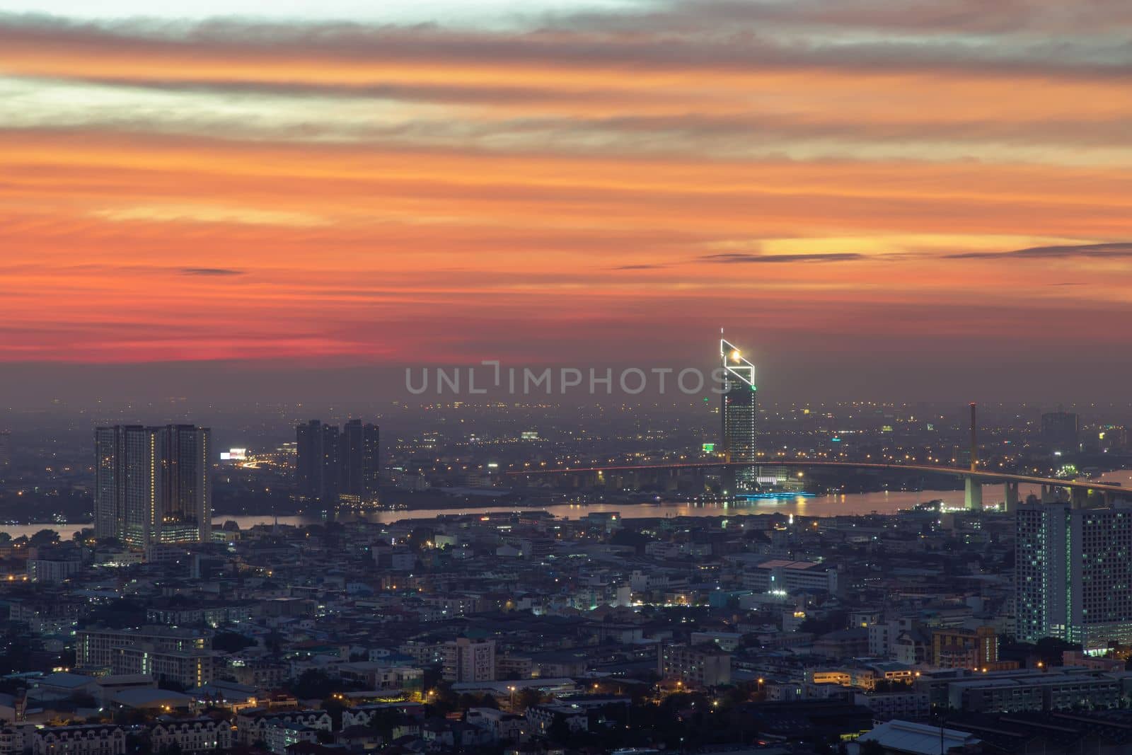 Bangkok, thailand - Dec 23, 2020 : Aerial view of Bangkok city Overlooking Skyscrapers and the Bridge crosses the Chao Phraya river with bright glowing lights at dusk. No focus, specifically.