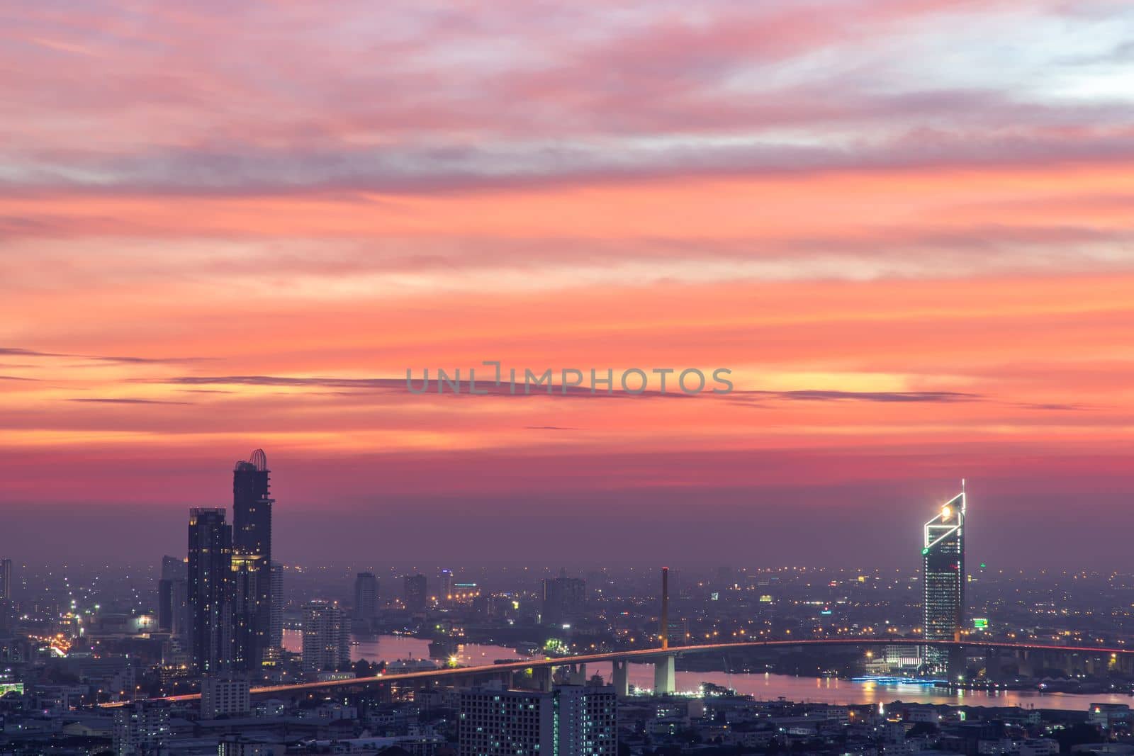 Bangkok, thailand - Dec 23, 2020 : Aerial view of Bangkok city Overlooking Skyscrapers and the Bridge crosses the Chao Phraya river with bright glowing lights at dusk. No focus, specifically.