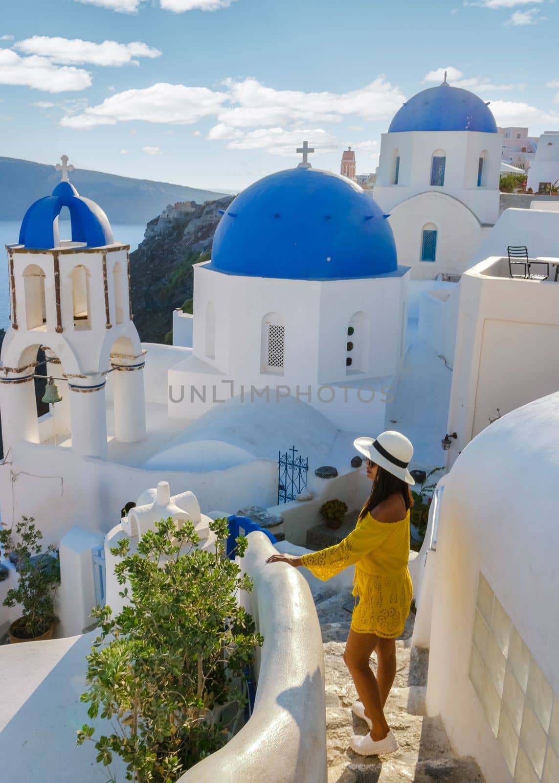 Happy Asian woman visit Oia Santorini Greece on a sunny day during summer with whitewashed homes and churches, Greek Island Aegean Cyclades