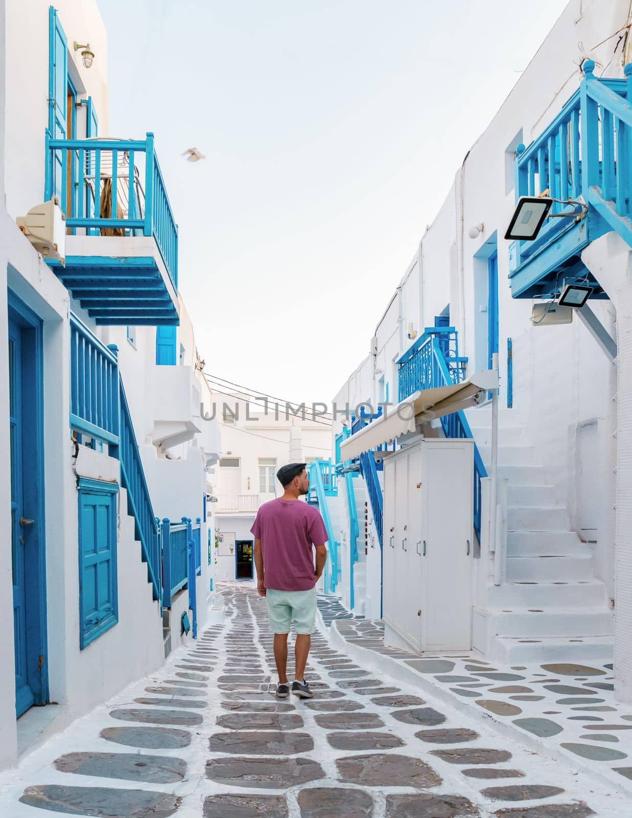 Young men visit Mykonos Greek village in Greece, colorful streets of Mikonos village by fokkebok