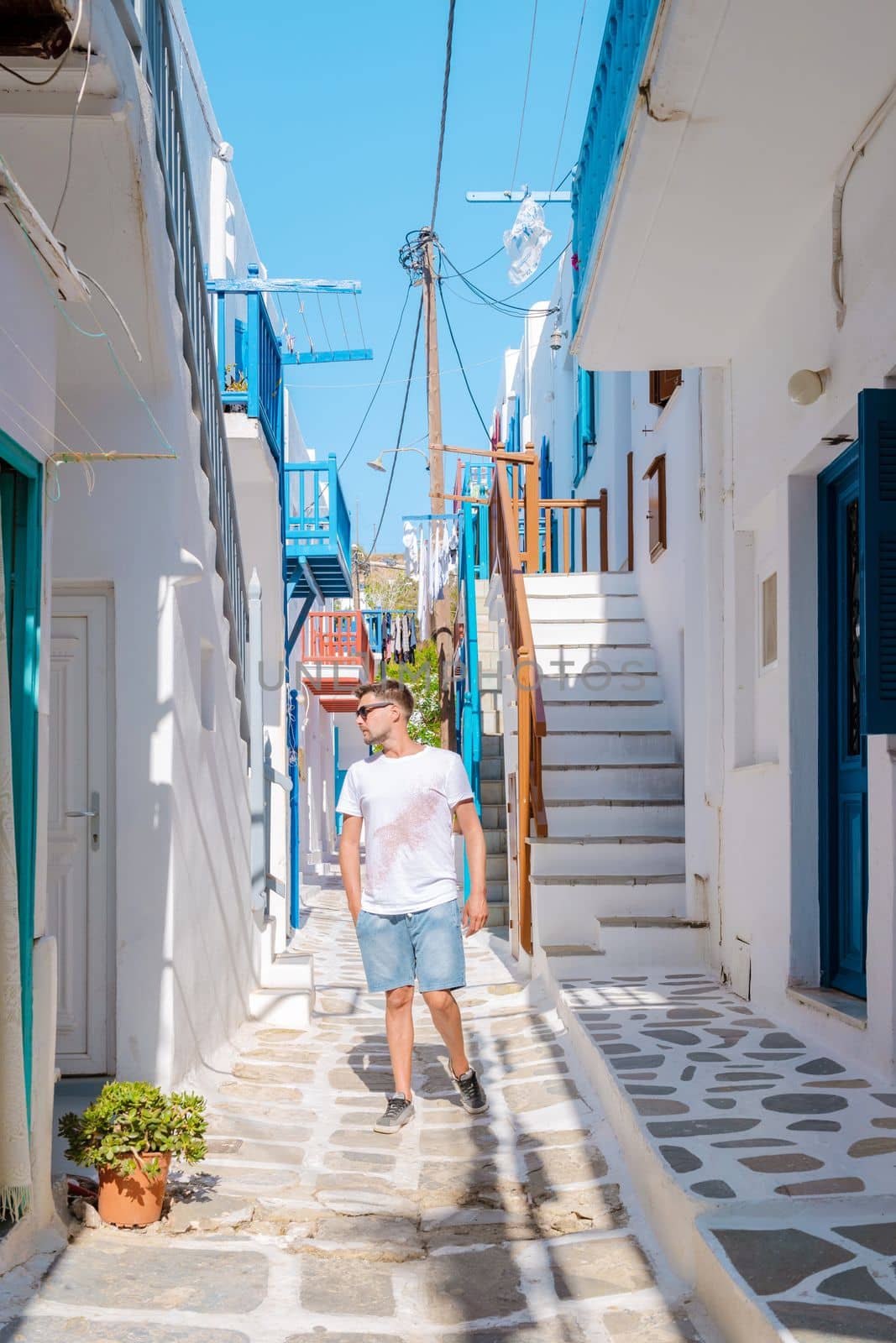 Young men visit Mykonos Greek village in Greece, colorful streets of Mikonos village by fokkebok