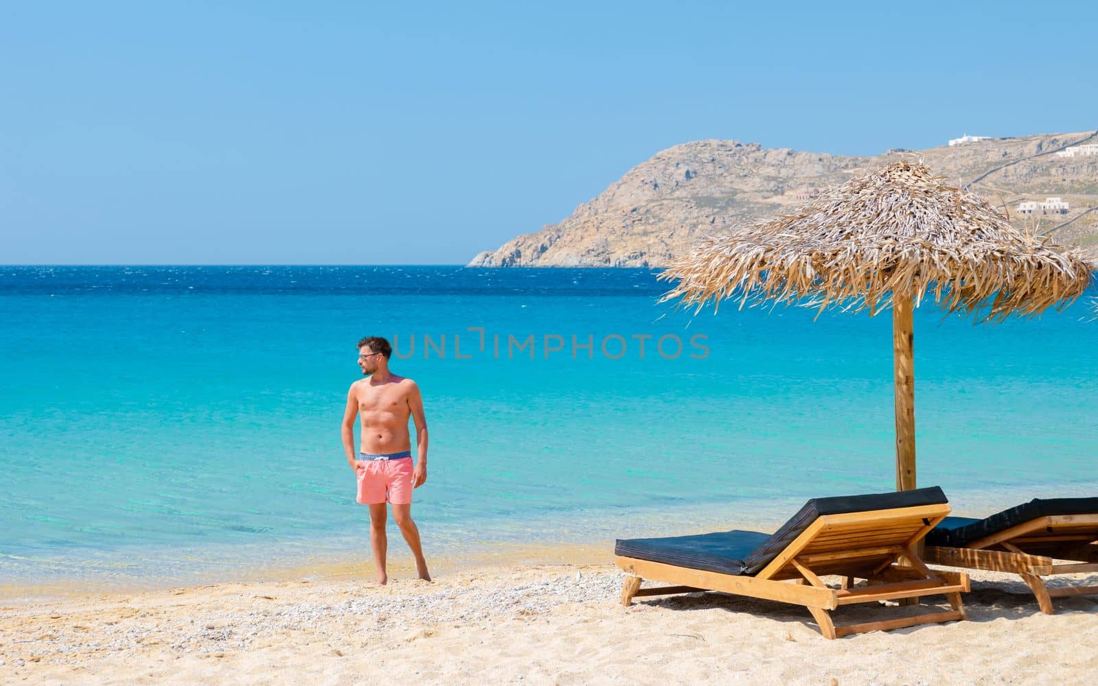 Young men on the beach with umbrella and luxury beach chairs at Elia beach Mykonos Greece by fokkebok