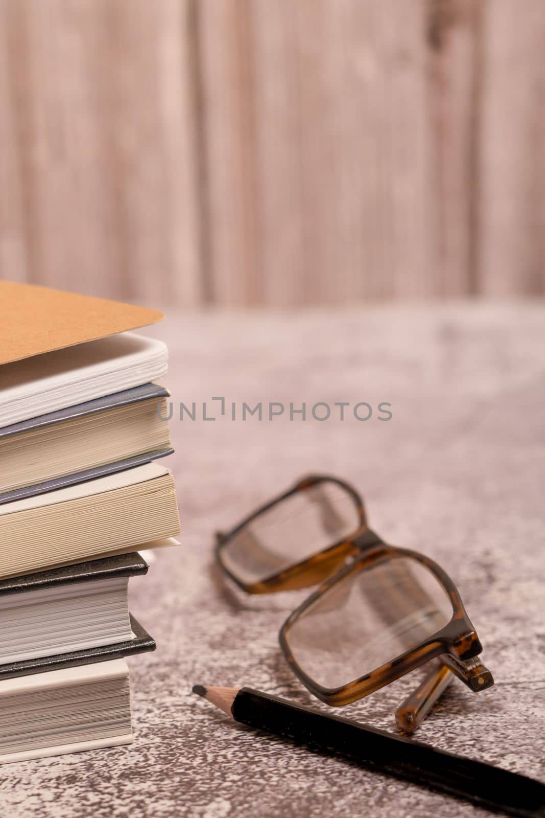 stack of old books with glasses and a black pencil with a blurred background