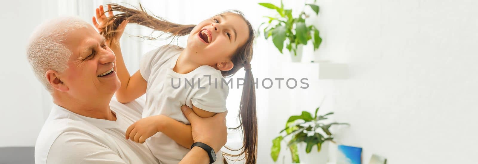 Middle-aged caucasian man playing with a little girl on the river bank. Man stands astoop ans holds his granddaughter on his back as she is "flying" Everybody's happy