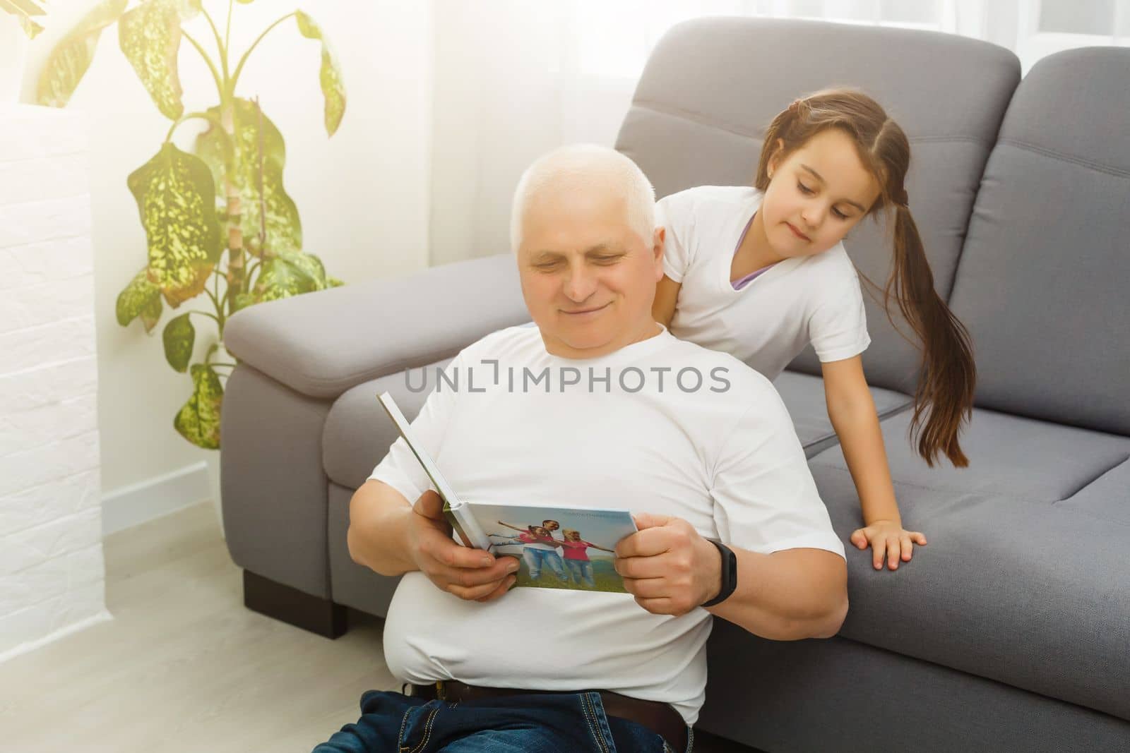 Happy little girl with grandfather watching photo books at home