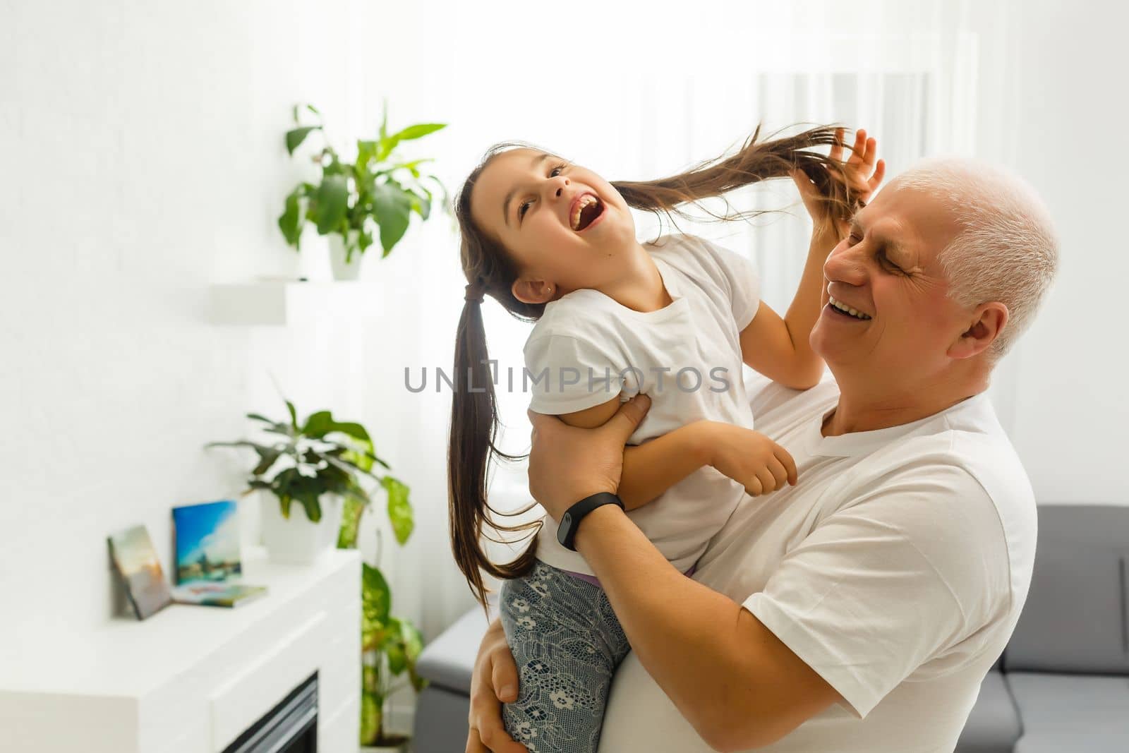 Middle-aged caucasian man playing with a little girl on the river bank. Man stands astoop ans holds his granddaughter on his back as she is "flying" Everybody's happy