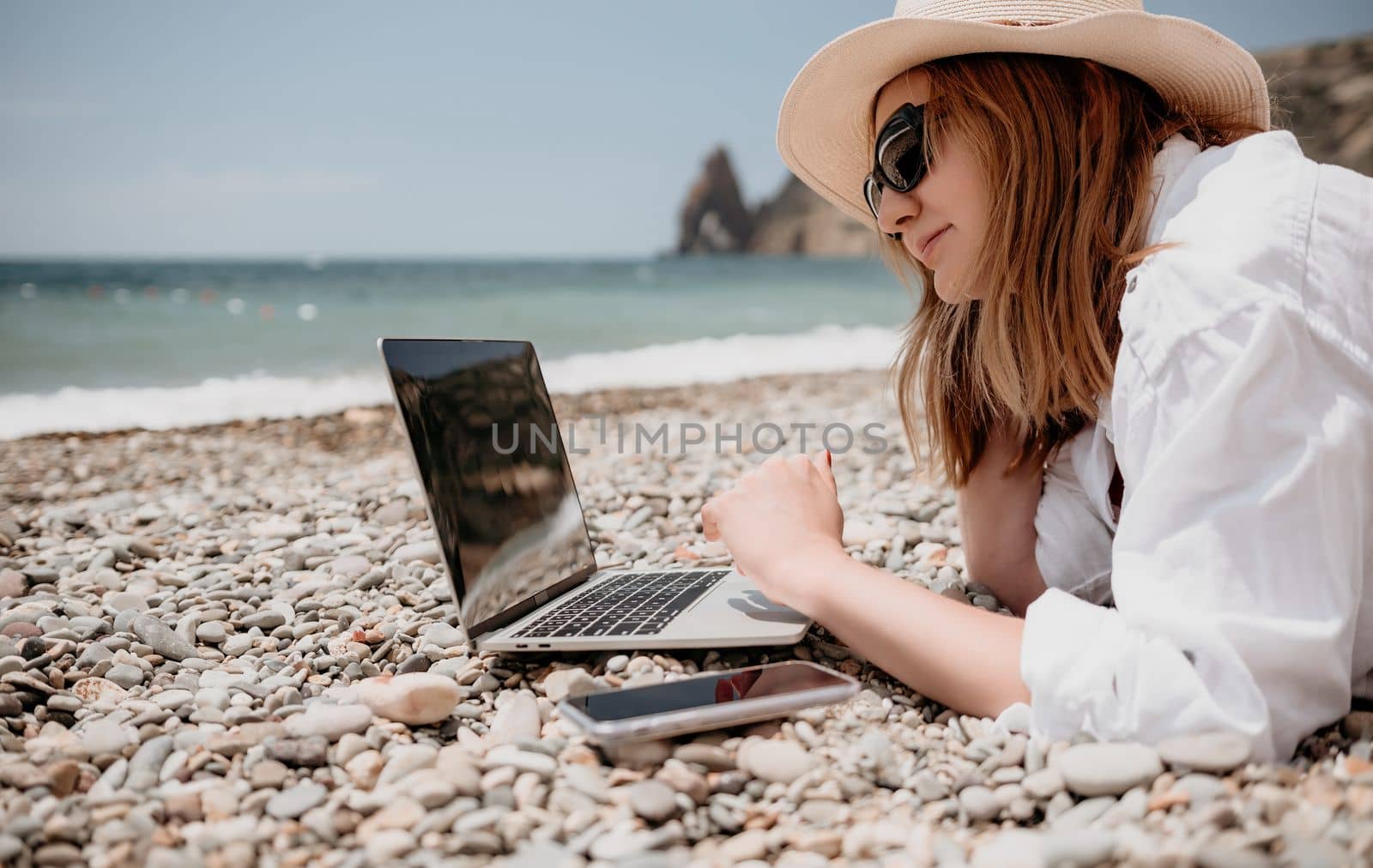 Woman sea laptop. Business woman in yellow hat working on laptop by sea. Close up on hands of pretty lady typing on computer outdoors summer day. Freelance, digital nomad, travel and holidays concept. by panophotograph