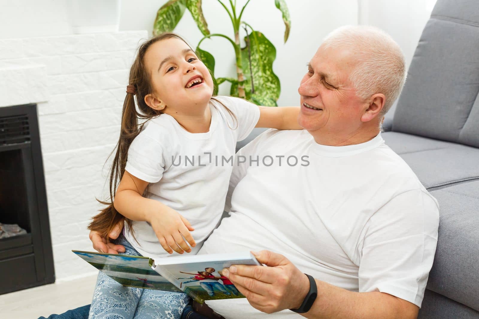Happy little girl with grandfather reading story book at home