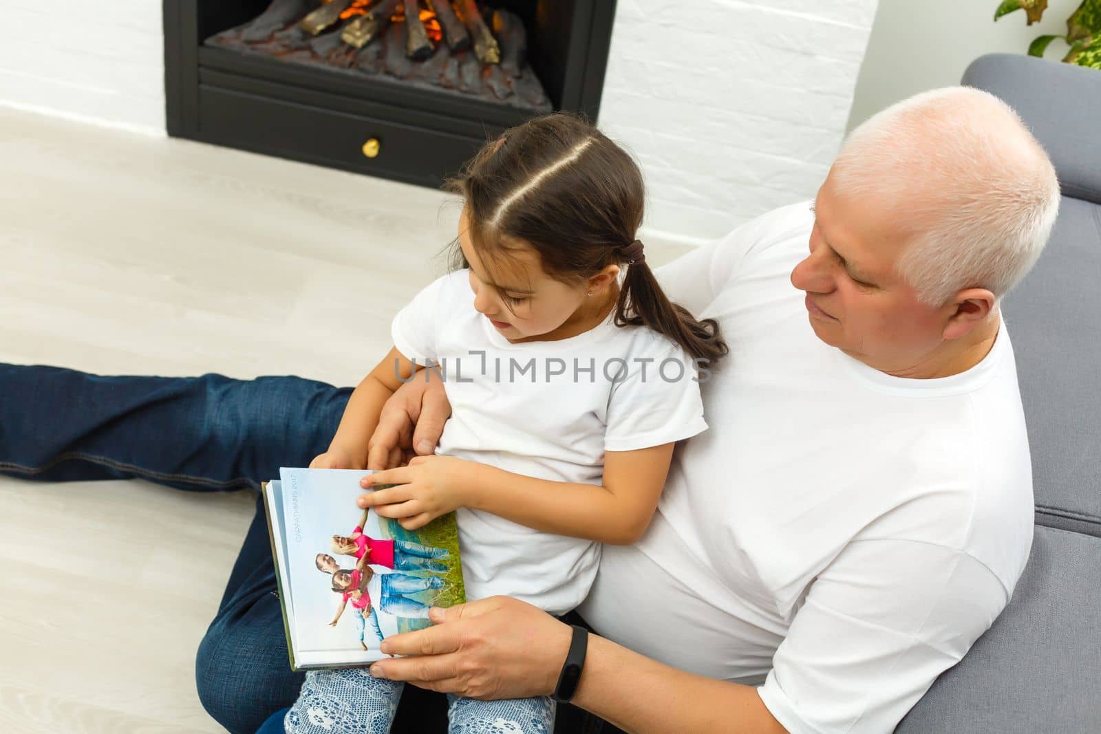 Happy little girl with grandfather watching photo books at home