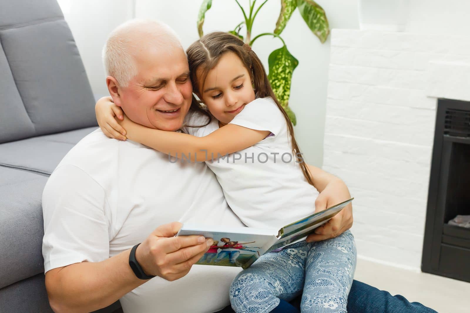 Happy little girl with grandfather watching photo books at home