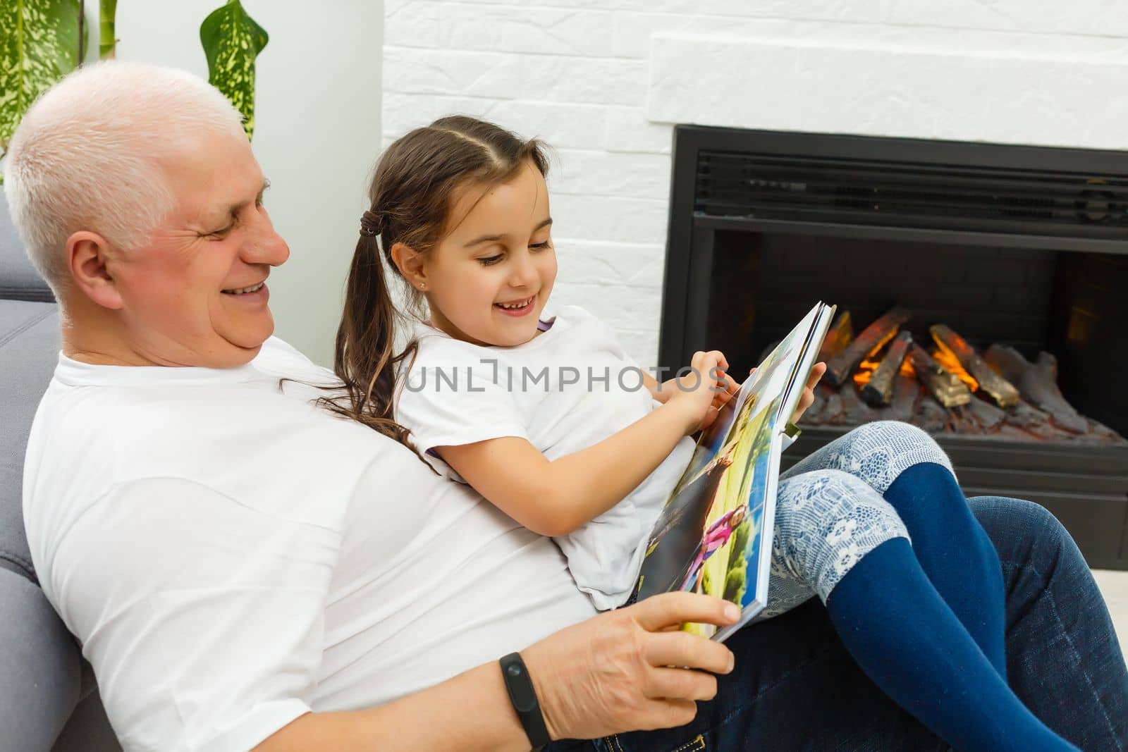 Happy little girl with grandfather reading story book at home