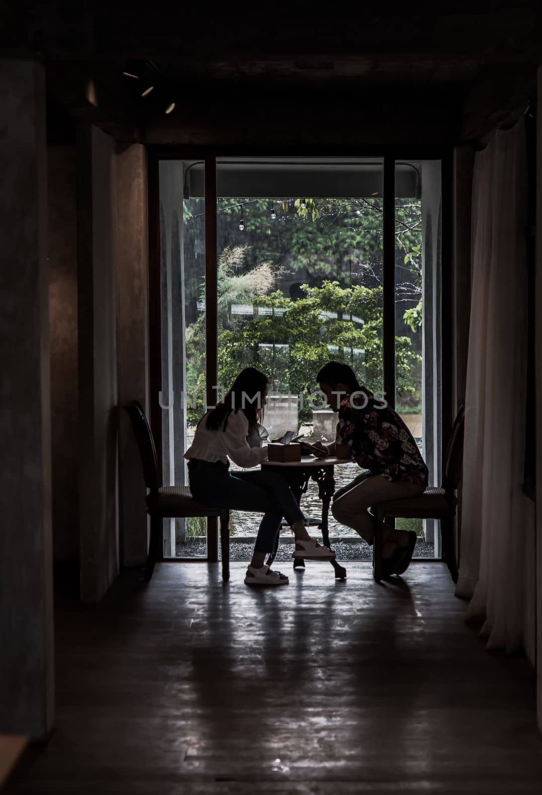 Chiang Mai,Thailand - Sep 07, 2020 : Shot of young adults sit and relaxing in a cafe and using mobile phone. Young man and woman at cozy coffee shop, Slow life concept. Dark tone, Focus and blur.