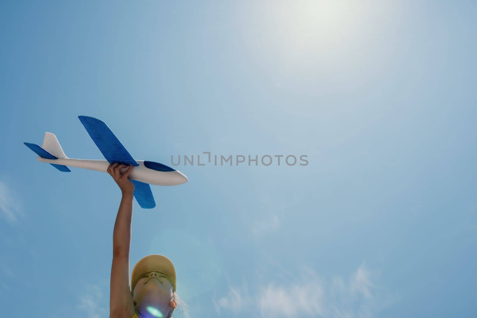 Kid playing with toy airplane. Children dream of travel by plane. Happy child girl has fun in summer vacation by sea and mountains. Outdoors activities at background of blue sky. Lifestyle moment
