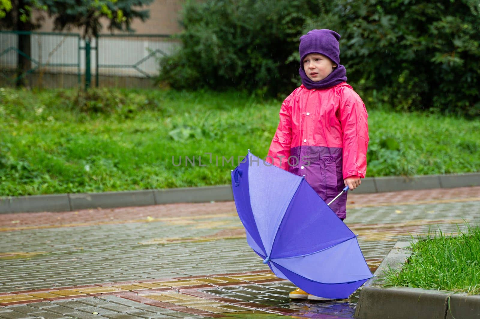 Child playing in autumn rain. Kid with umbrella. Outdoor fun for kids by any weather. Rain waterproof wear, boots and jacket for children.