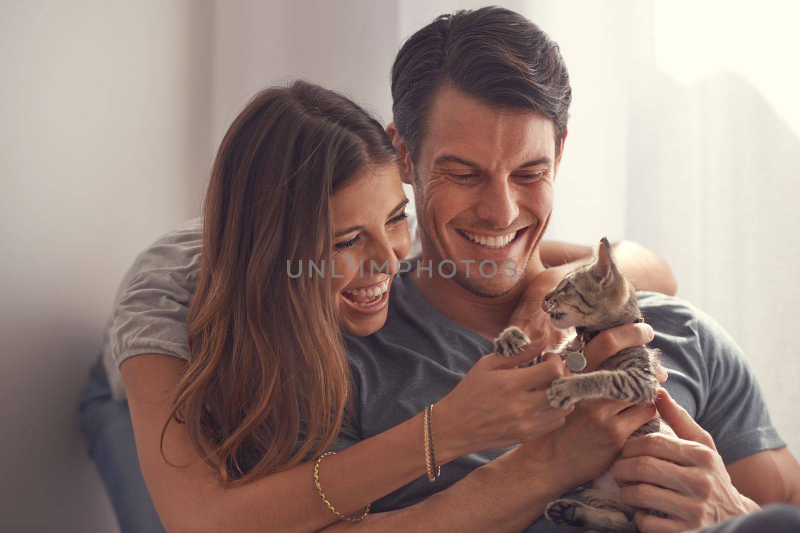 Cuddles and cuteness. a loving young couple sitting with their kitten. by YuriArcurs