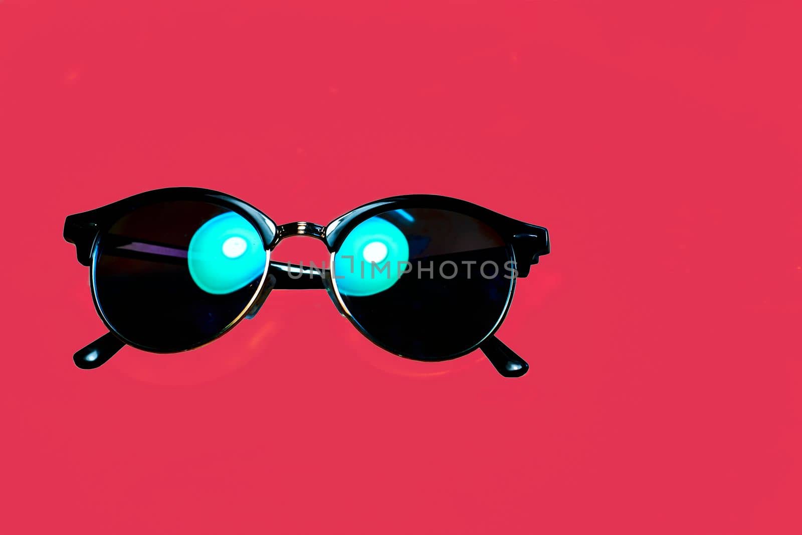 glasses tinted to protect the eyes from sunlight or glare. Black sunglasses with emerald highlights on a red background