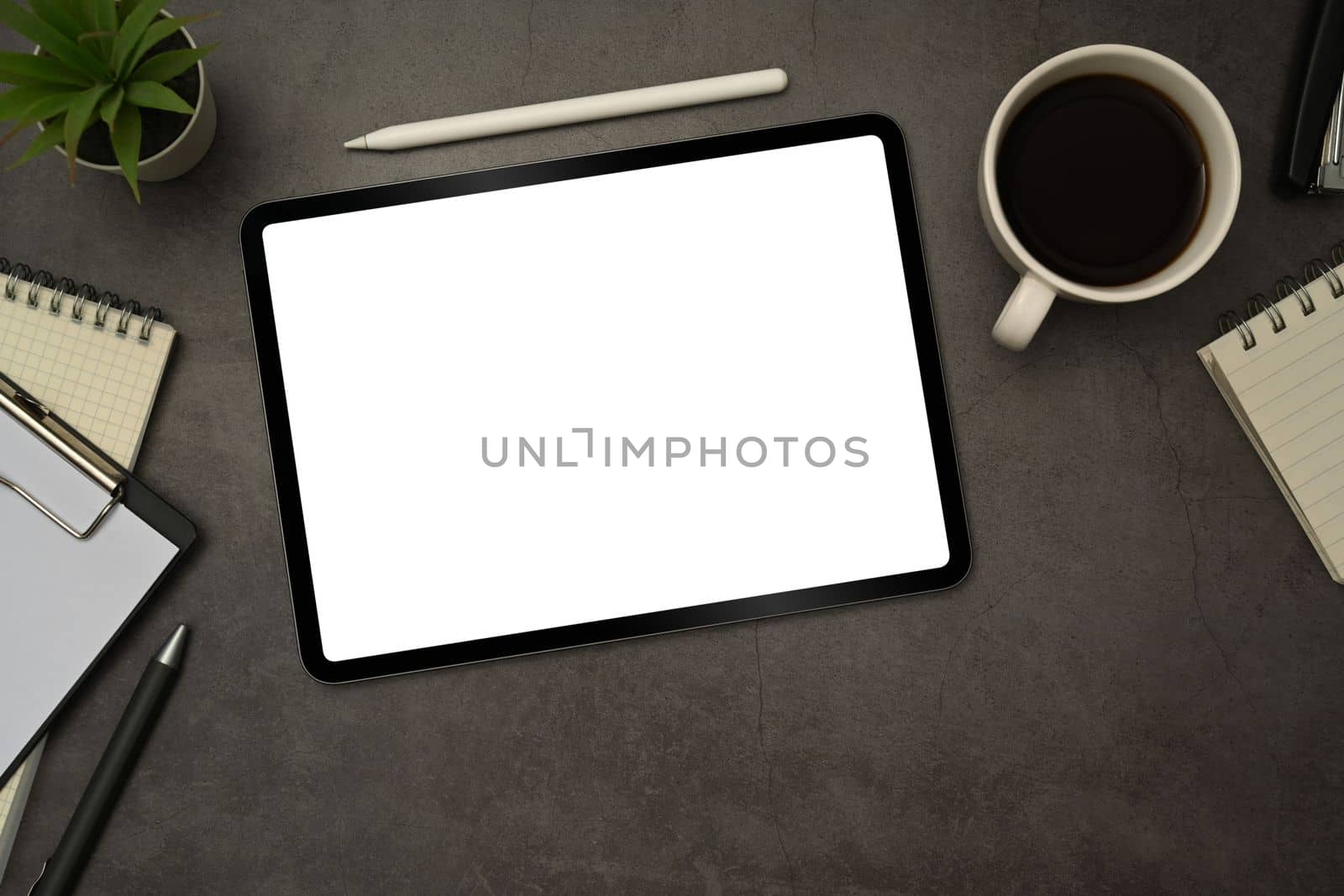 Flat lay digital tablet with white empty display, stylus pen, coffee cup and notepad on black slate texture background by prathanchorruangsak