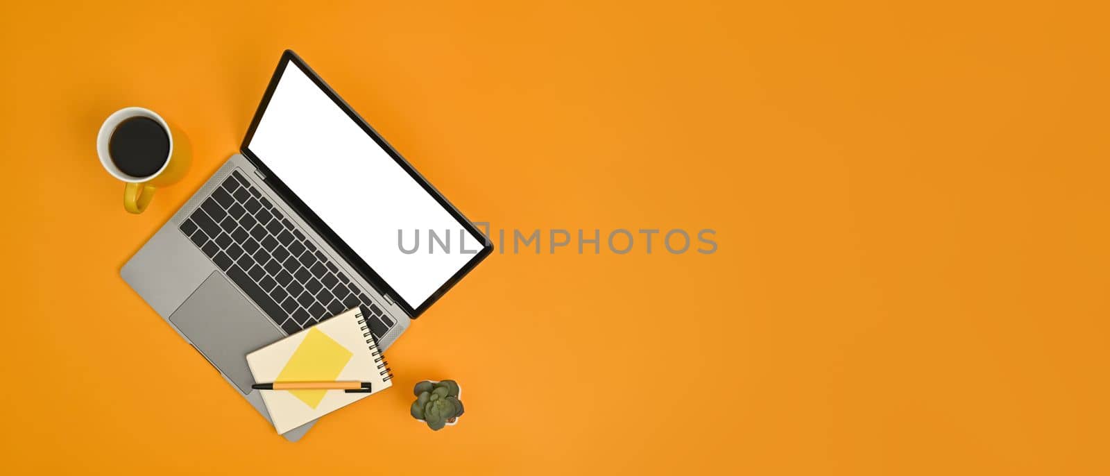 Mock up laptop computer with blank screen, notepad and coffee cup on yellow background. Copy space for your advertise text by prathanchorruangsak