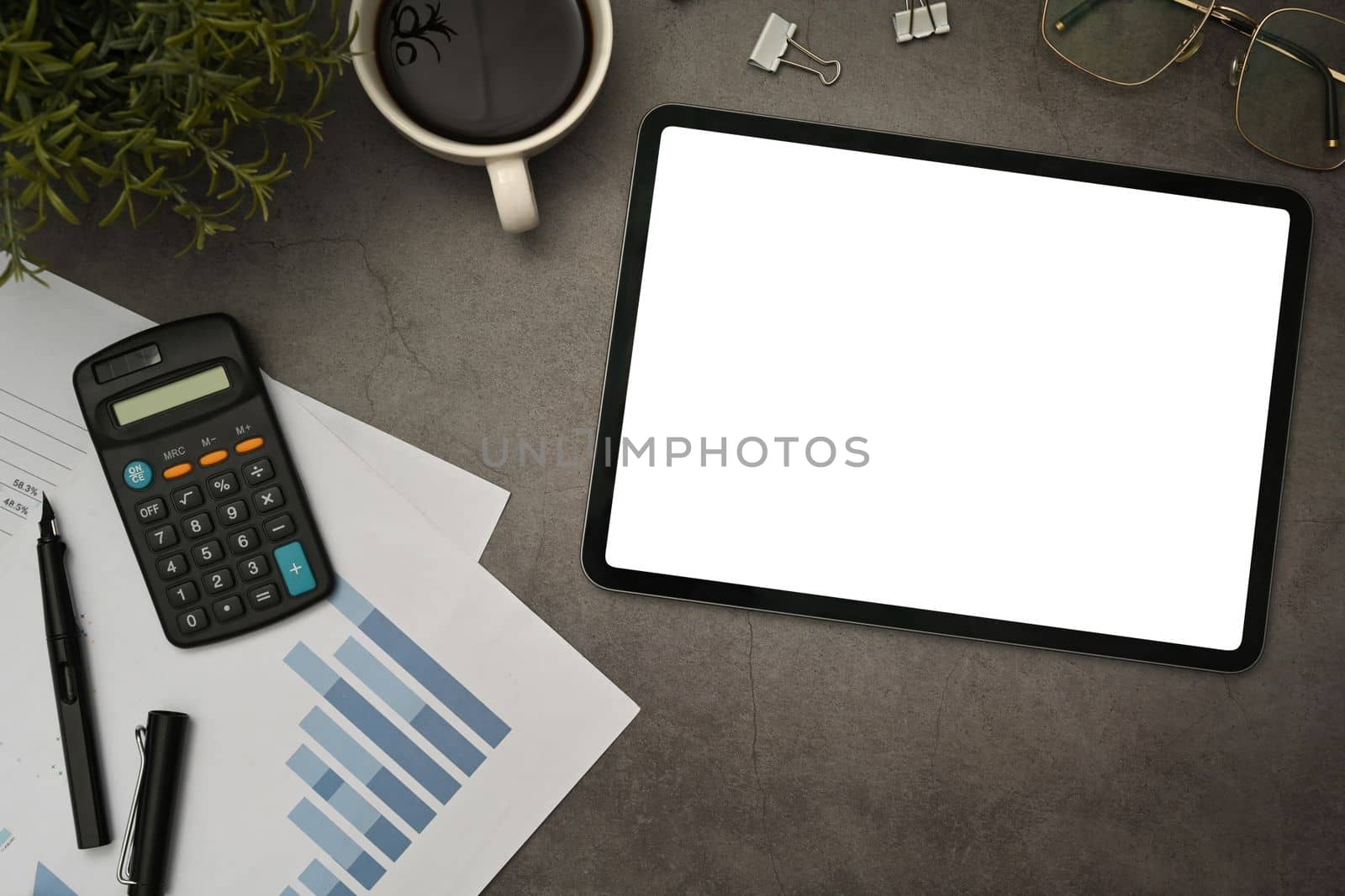 Tablet with empty display, calculator, financial reports and supplies on black slate texture background.