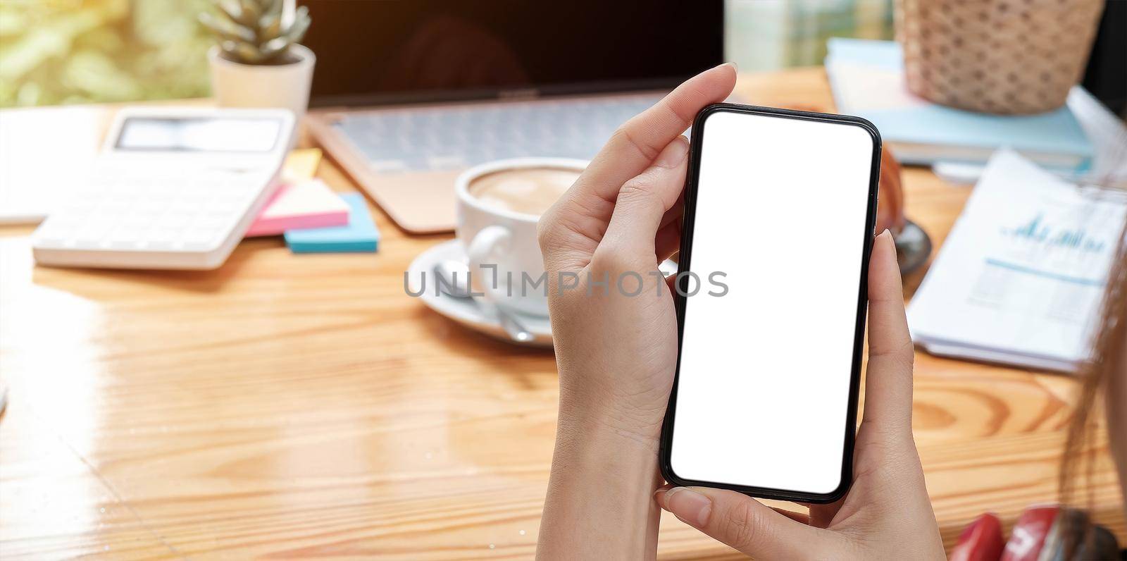 Mockup image blank white screen cell phone.women hand holding texting using mobile on desk at home office..
