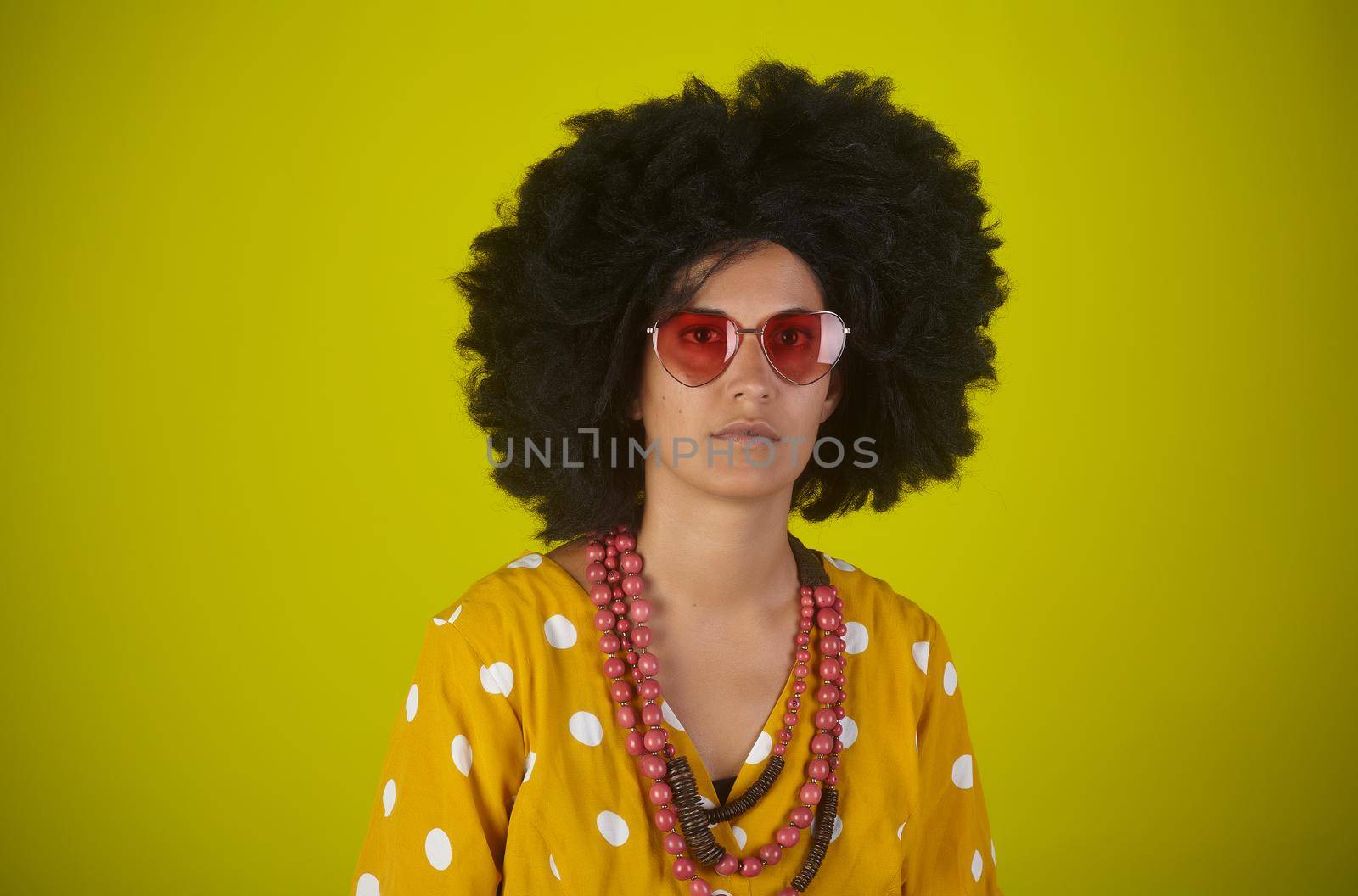 A beautiful woman with the curly afro hairstyle wearing sunglasses on yellow background by bepsimage