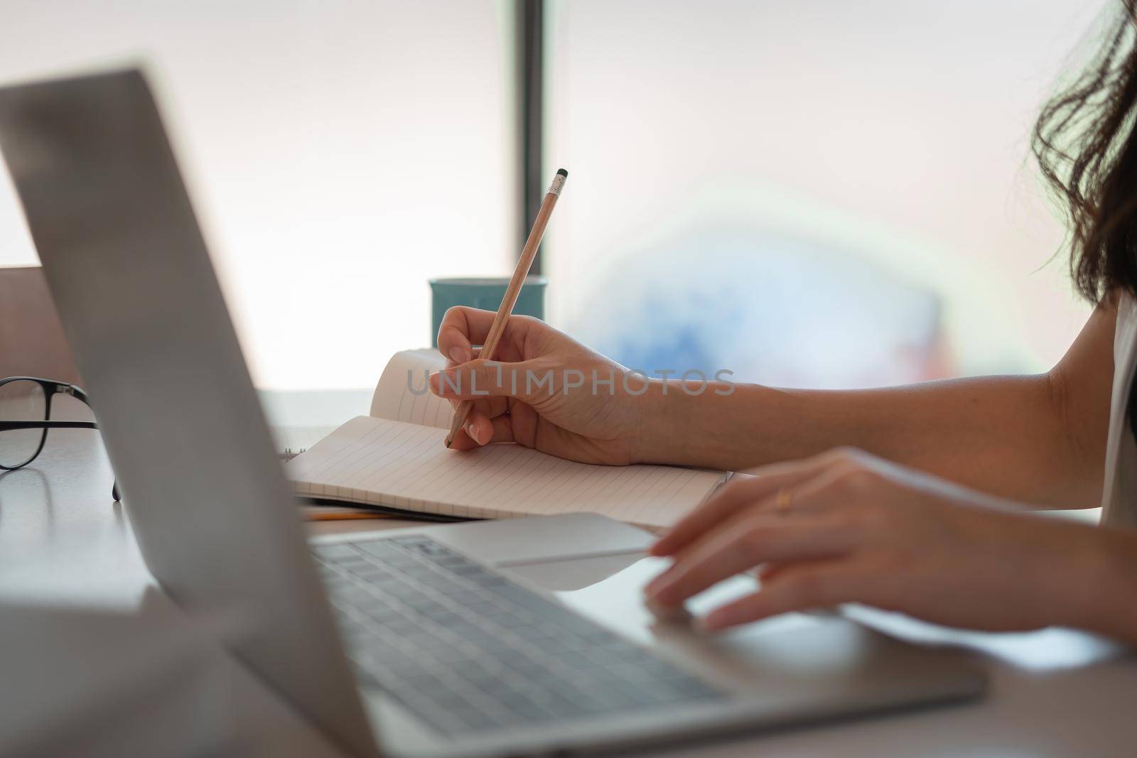 Close up woman's hands with laptop computer, notebook and pen taking notes in business office.