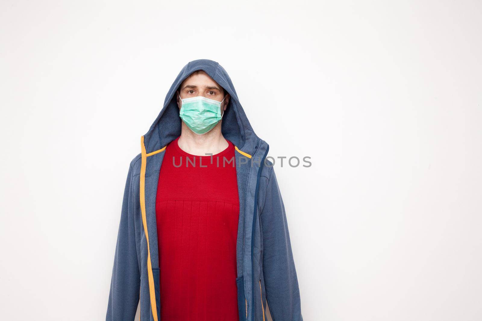 Man with green protective mask on white background. A man with a red sweater and a blue jacket, with a hood.