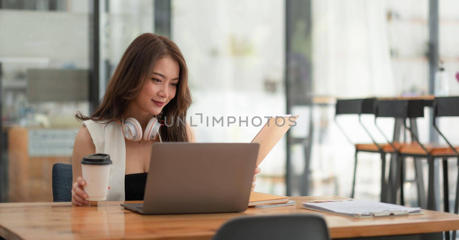 Smiling girl student wear wireless headphone study online with teacher, happy young asian woman learn language listen lecture watch webinar write notes look at laptop sit in cafe, distant education. by nateemee